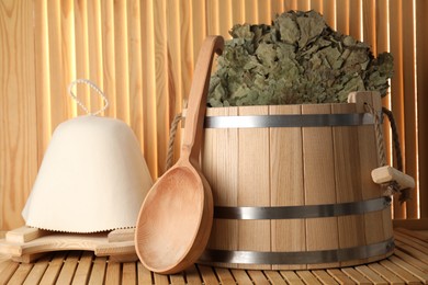 Photo of Sauna equipment. Bucket, ladle, oak whisk and felt wool hat on wooden surface