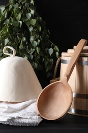 Photo of Sauna equipment. Wooden bucket, towel, felt wool hat and ladle on black surface