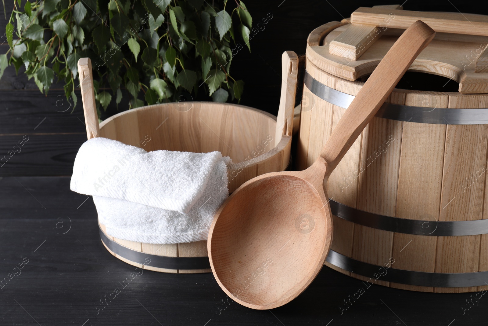 Photo of Sauna equipment. Wooden buckets, towel and ladle on black surface