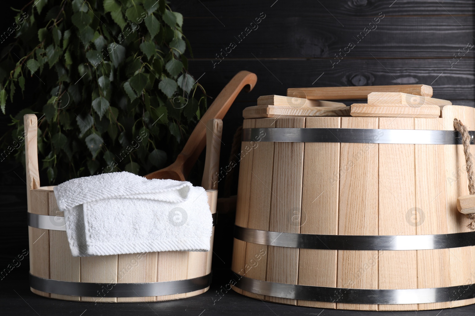 Photo of Sauna equipment. Wooden buckets, towel and ladle on black surface