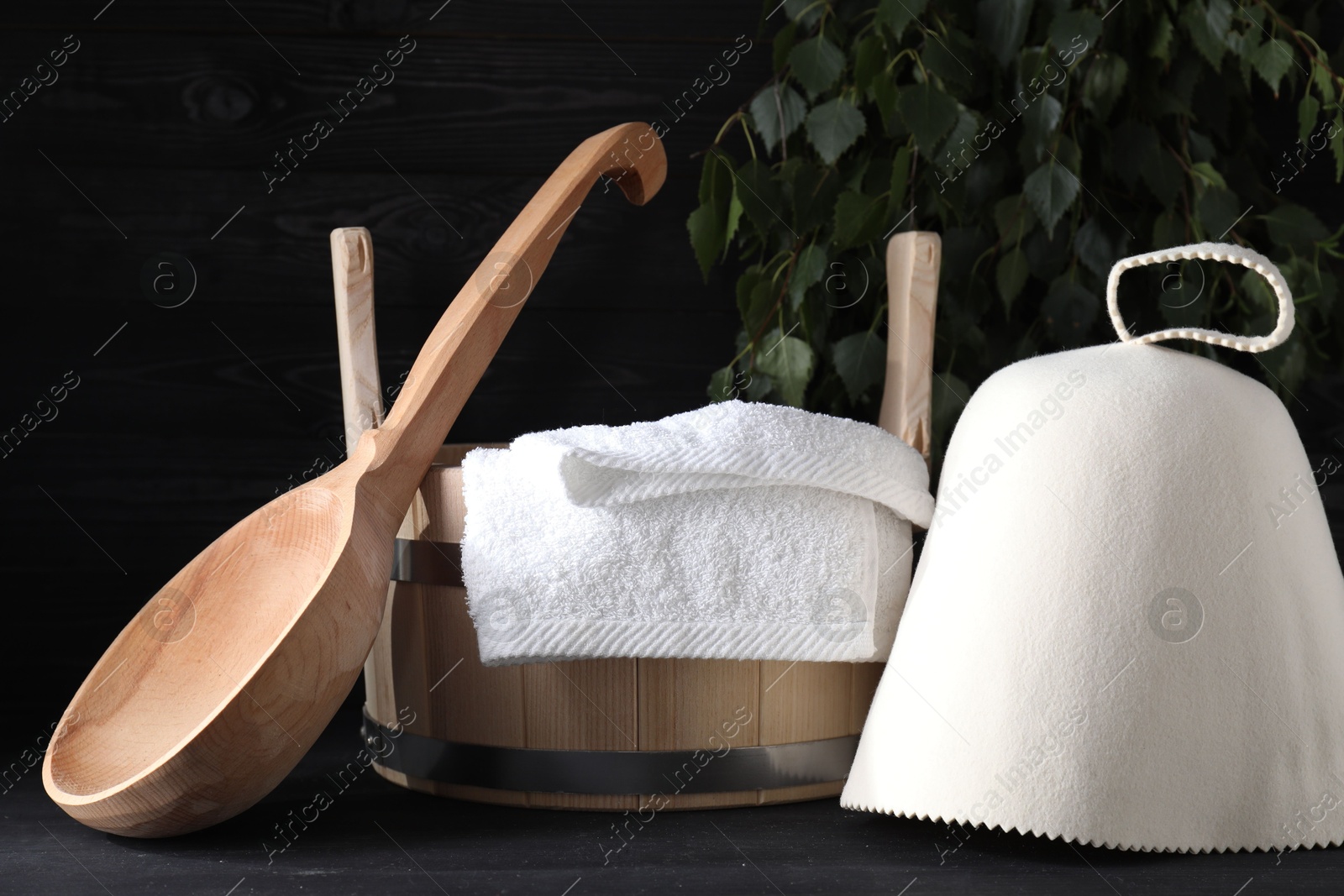 Photo of Sauna equipment. Felt wool hat, wooden bucket, towel and ladle on black table