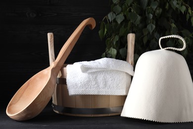 Sauna equipment. Felt wool hat, wooden bucket, towel and ladle on black table