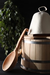 Photo of Sauna equipment. Felt wool hat, wooden bucket and ladle on black table