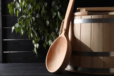 Sauna equipment. Wooden ladle and bucket on black table, space for text