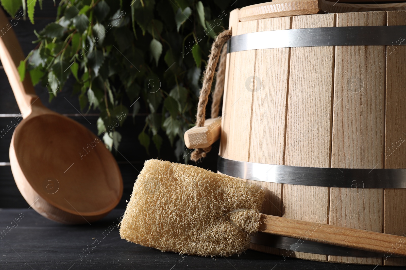 Photo of Sauna equipment. Wooden bucket, ladle and loofah on black table