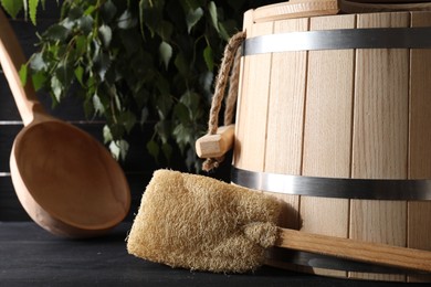 Photo of Sauna equipment. Wooden bucket, ladle and loofah on black table