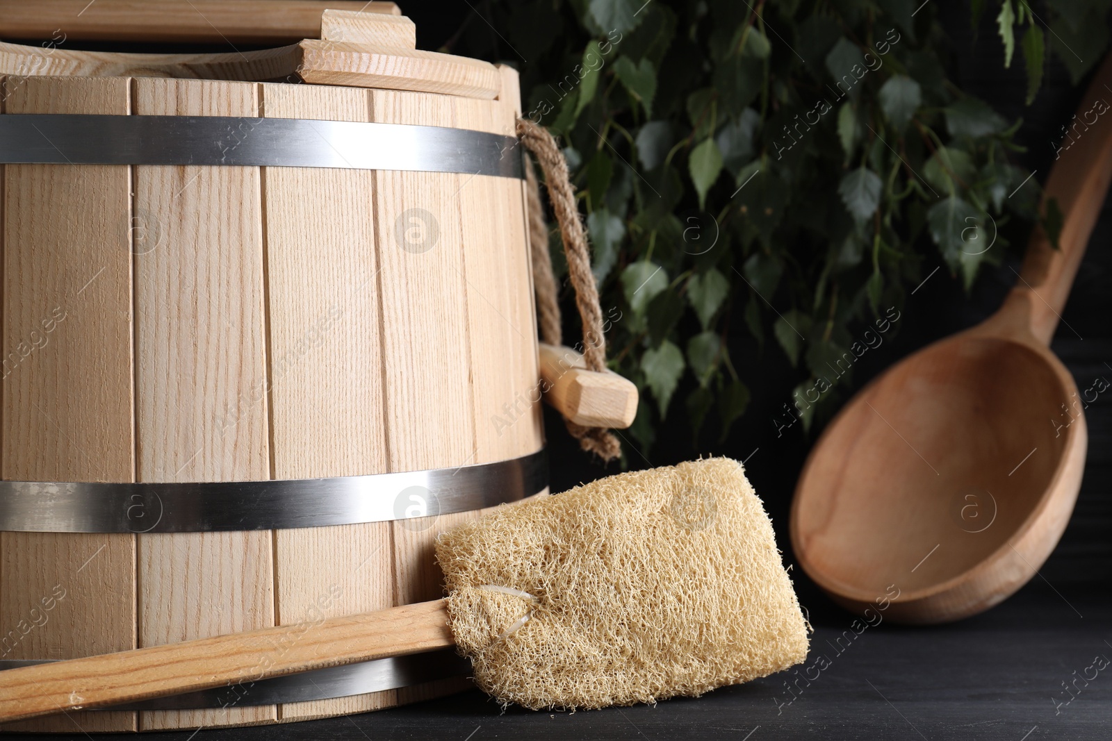 Photo of Sauna equipment. Wooden bucket, ladle and loofah on black table