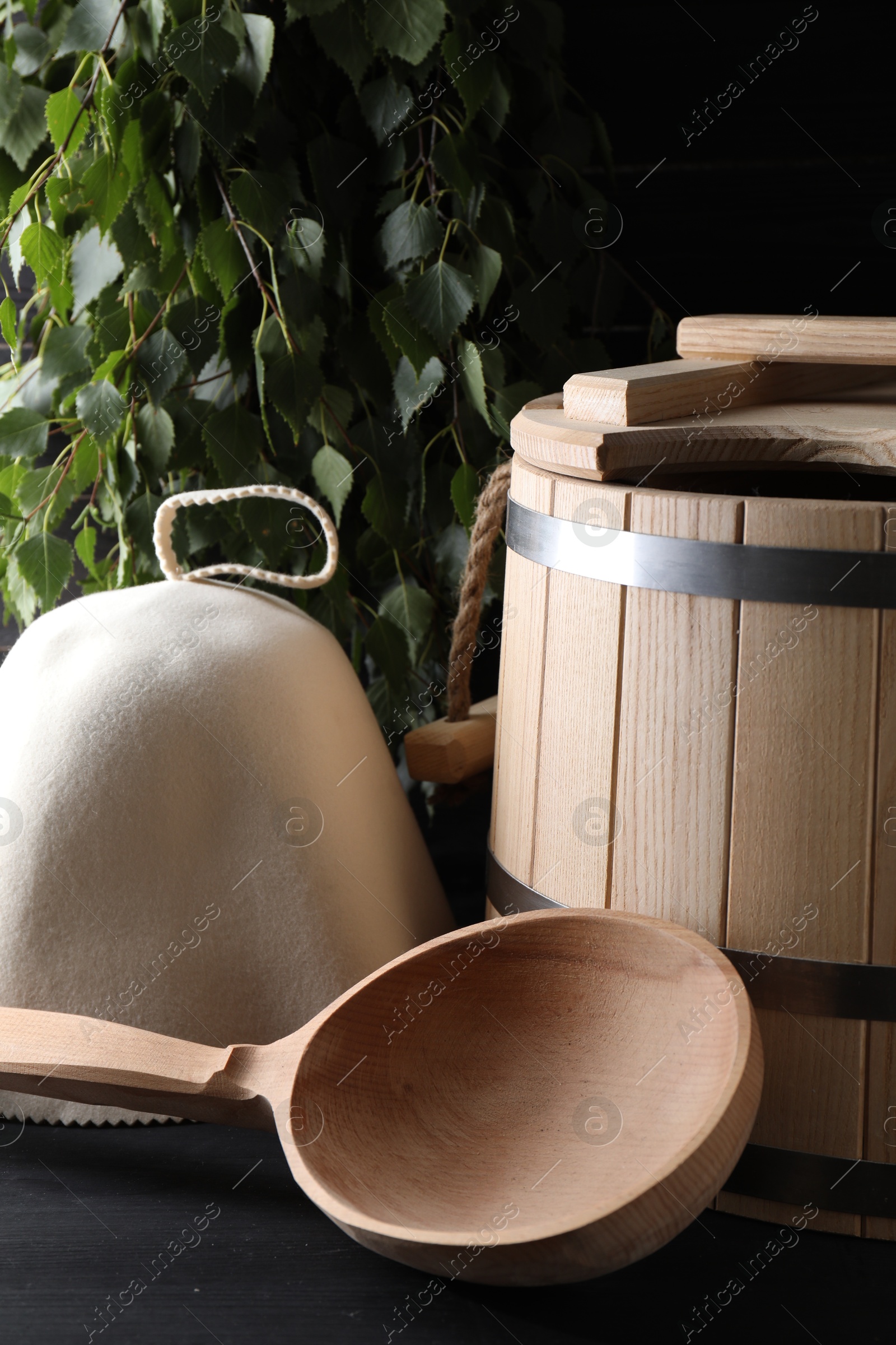 Photo of Sauna equipment. Felt wool hat, wooden bucket and ladle on black table