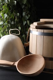 Photo of Sauna equipment. Felt wool hat, wooden bucket and ladle on black table