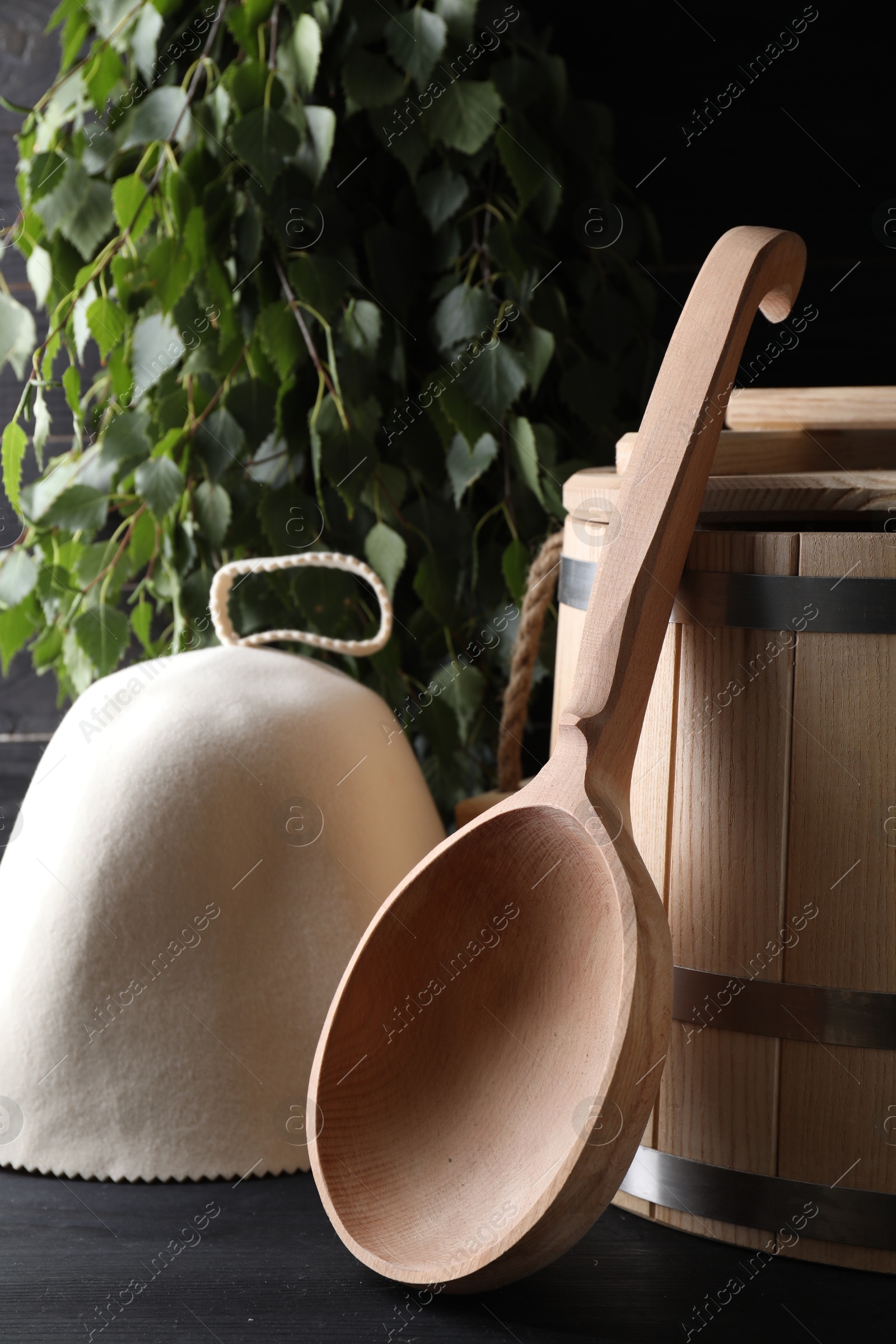 Photo of Sauna equipment. Felt wool hat, wooden bucket and ladle on black table