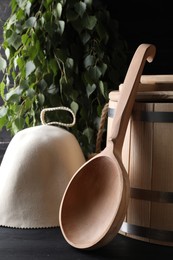 Photo of Sauna equipment. Felt wool hat, wooden bucket and ladle on black table