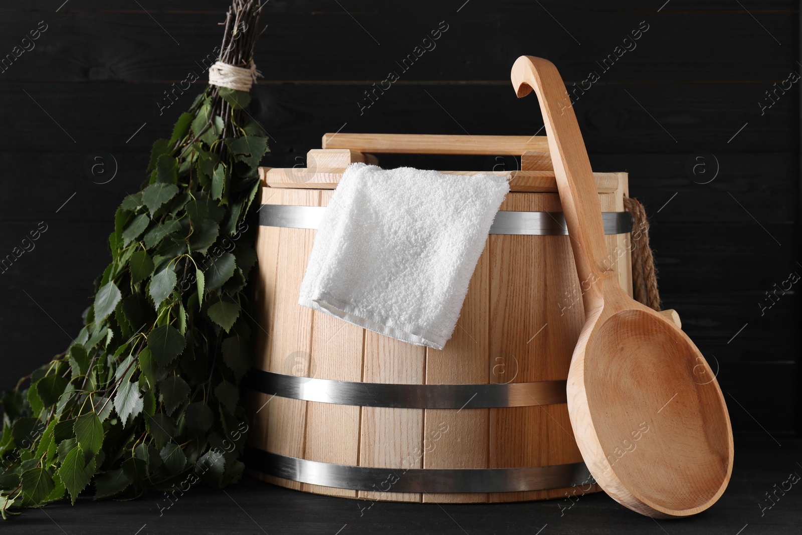 Photo of Sauna equipment. Wooden bucket, towel, ladle and oak whisk on black table