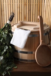 Photo of Sauna equipment. Bucket, towel, ladle and oak whisk on wooden table