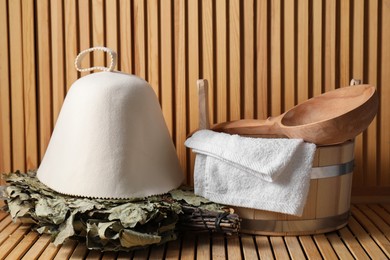 Oak sauna whisk, felt wool hat, bucket, towel and ladle on wooden surface