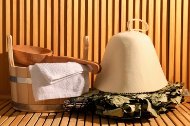 Oak sauna whisk, felt wool hat, bucket, towel and ladle on wooden surface