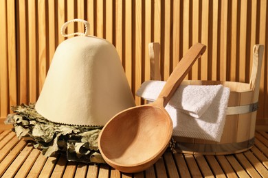 Oak sauna whisk, felt wool hat, bucket, towel and ladle on wooden surface