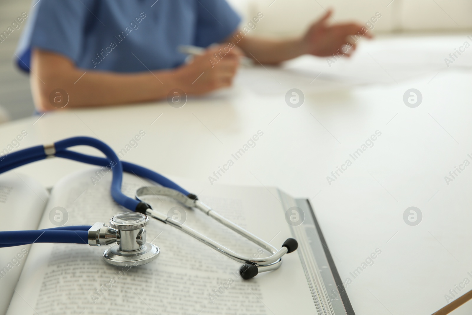 Photo of Doctor at white table in hospital, focus on medical stethoscope and book