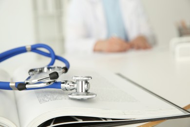 Photo of Doctor at table in hospital, focus on medical stethoscope and book