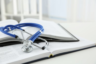 One medical stethoscope and books on white table, closeup