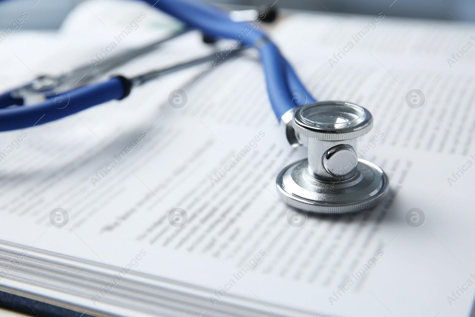 Photo of One medical stethoscope and book on table, closeup