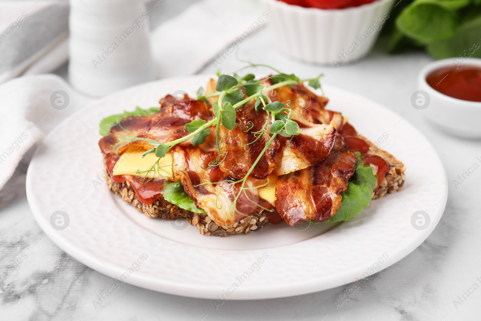 Photo of Tasty sandwich with bacon and microgreens on white marble table, closeup