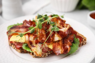 Photo of Tasty sandwich with bacon and microgreens on white table, closeup