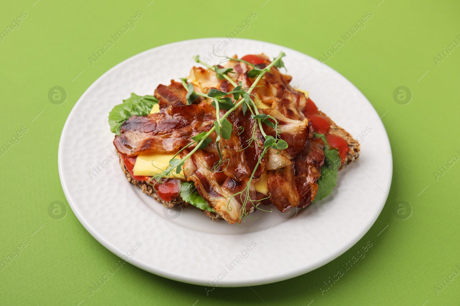 Photo of Tasty sandwich with bacon and microgreens on green table