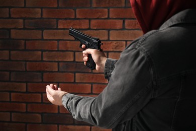 Photo of Dangerous criminal with gun near brick wall, closeup. Armed robbery