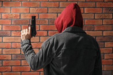 Photo of Dangerous criminal with gun near brick wall, back view. Armed robbery