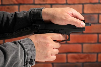 Dangerous criminal with gun near brick wall, closeup. Armed robbery