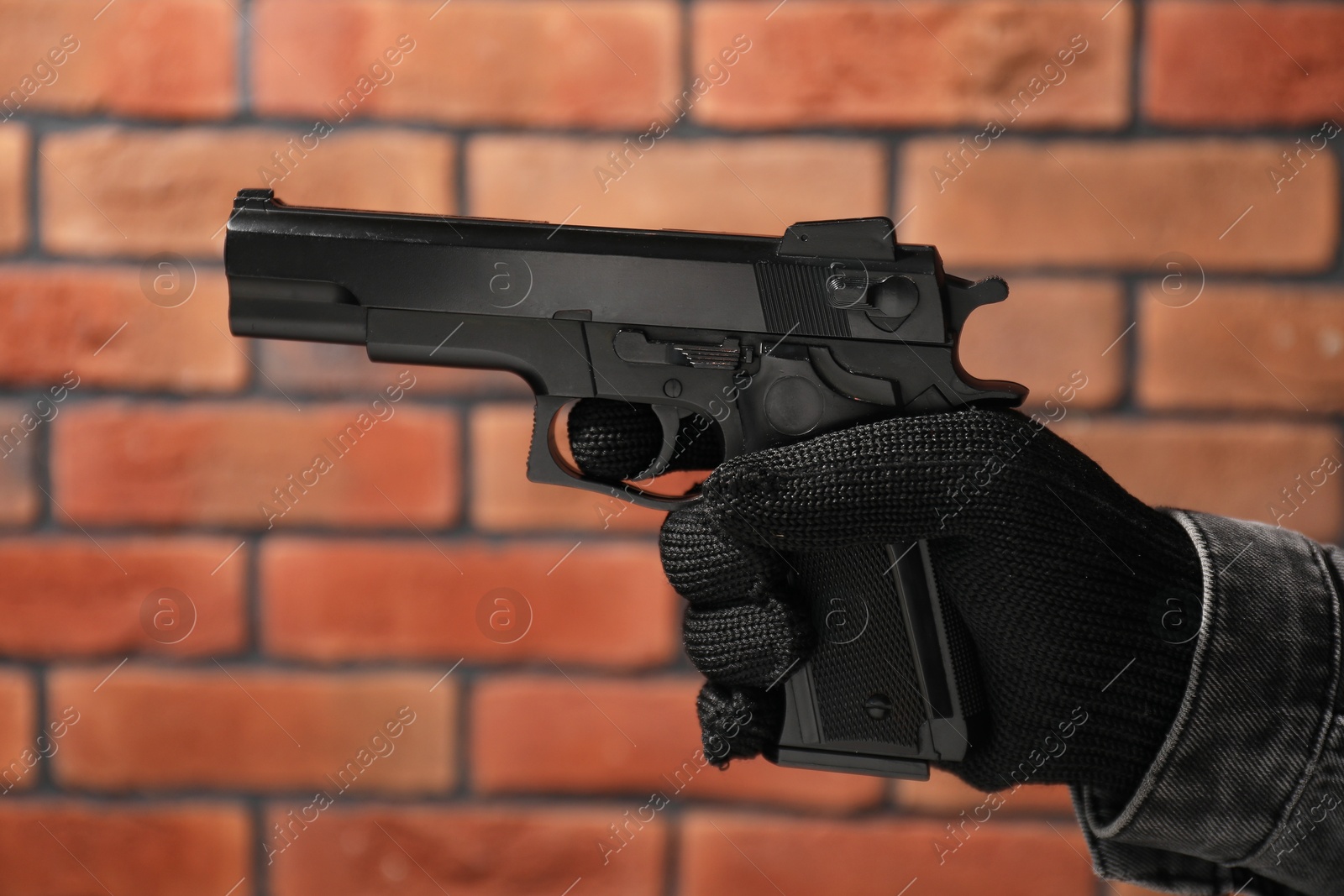 Photo of Dangerous criminal with gun near brick wall, closeup. Armed robbery