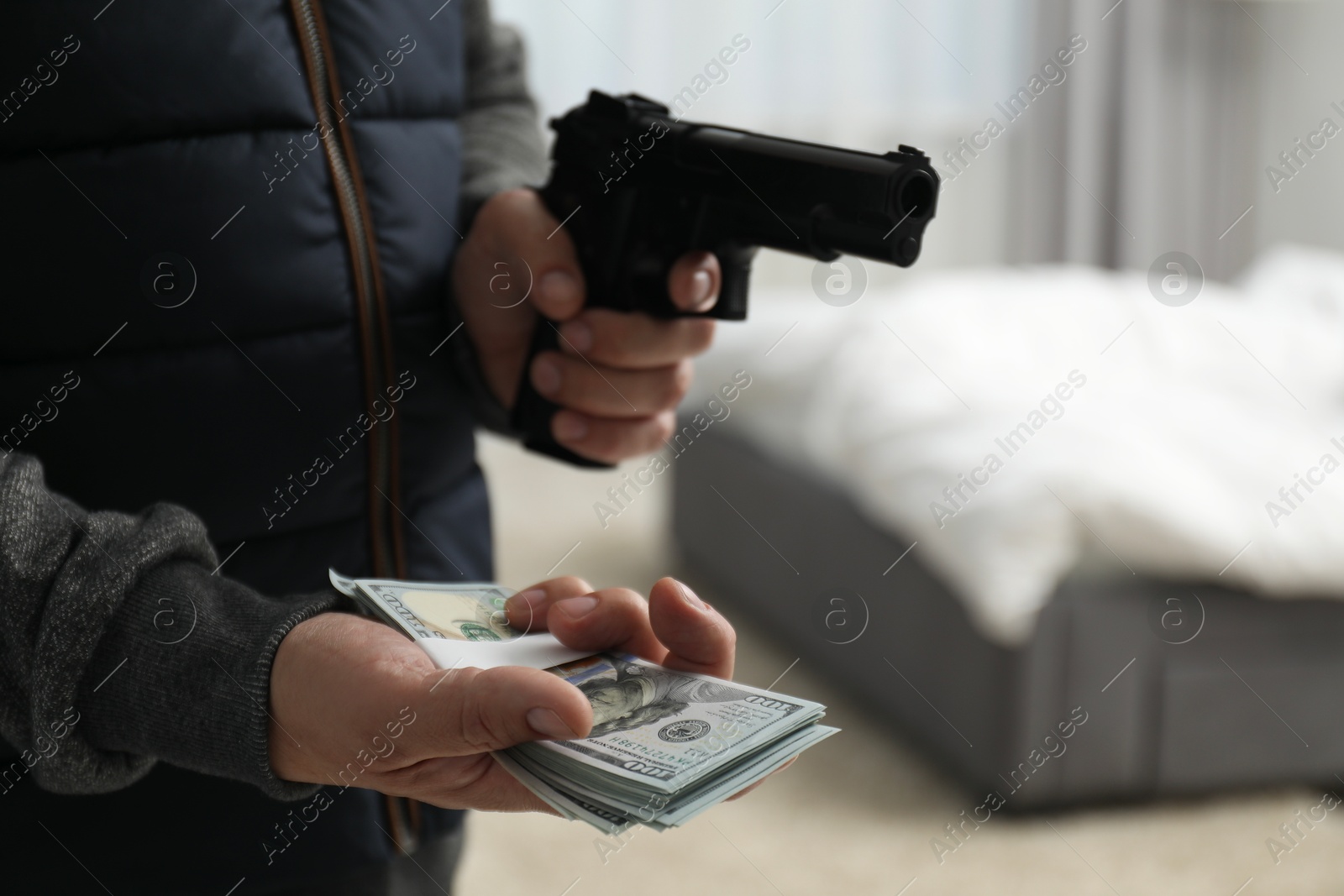 Photo of Dangerous criminal with gun holding money in foreign house, closeup. Armed robbery