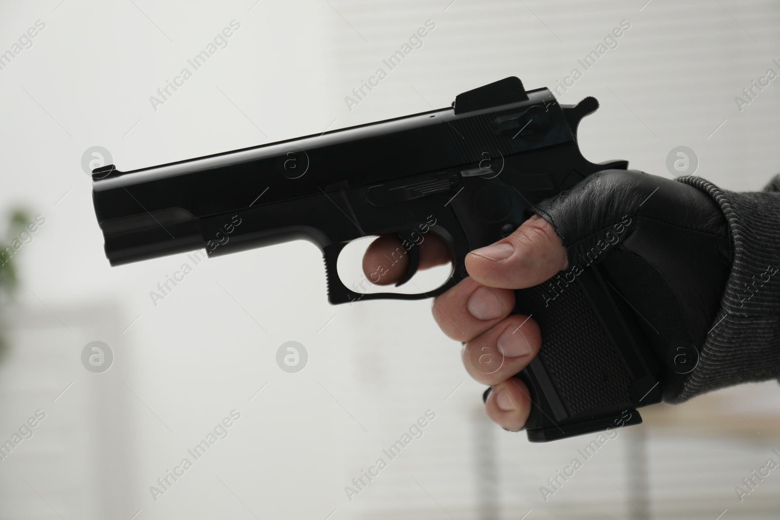 Photo of Dangerous criminal with gun indoors, closeup. Armed robbery