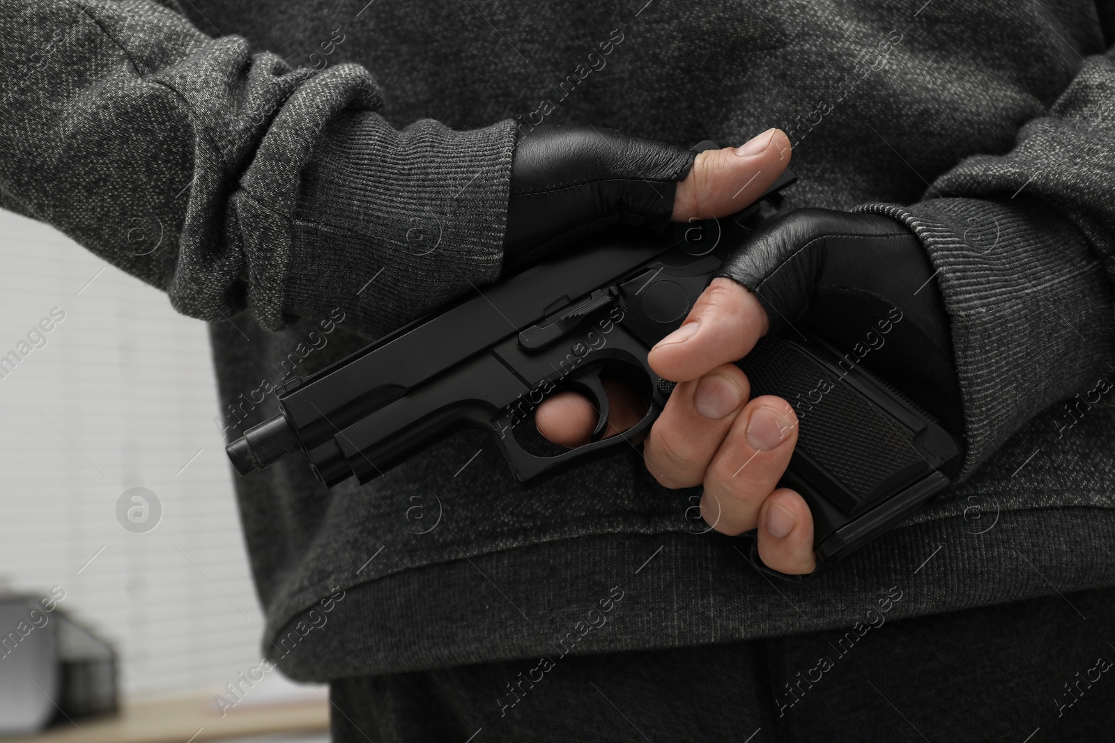 Photo of Man hiding gun behind his back indoors, closeup. Armed robbery