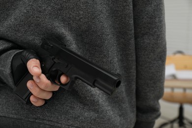 Photo of Man hiding gun behind his back indoors, closeup. Armed robbery