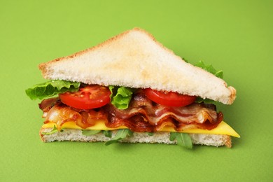 Delicious sandwich with fried bacon on green background, closeup