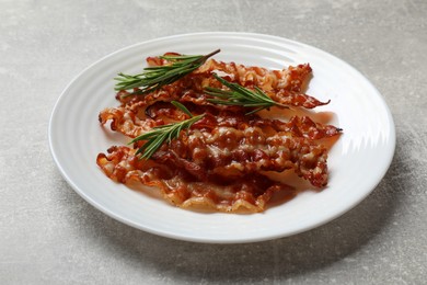 Photo of Slices of tasty fried bacon and rosemary on light grey table