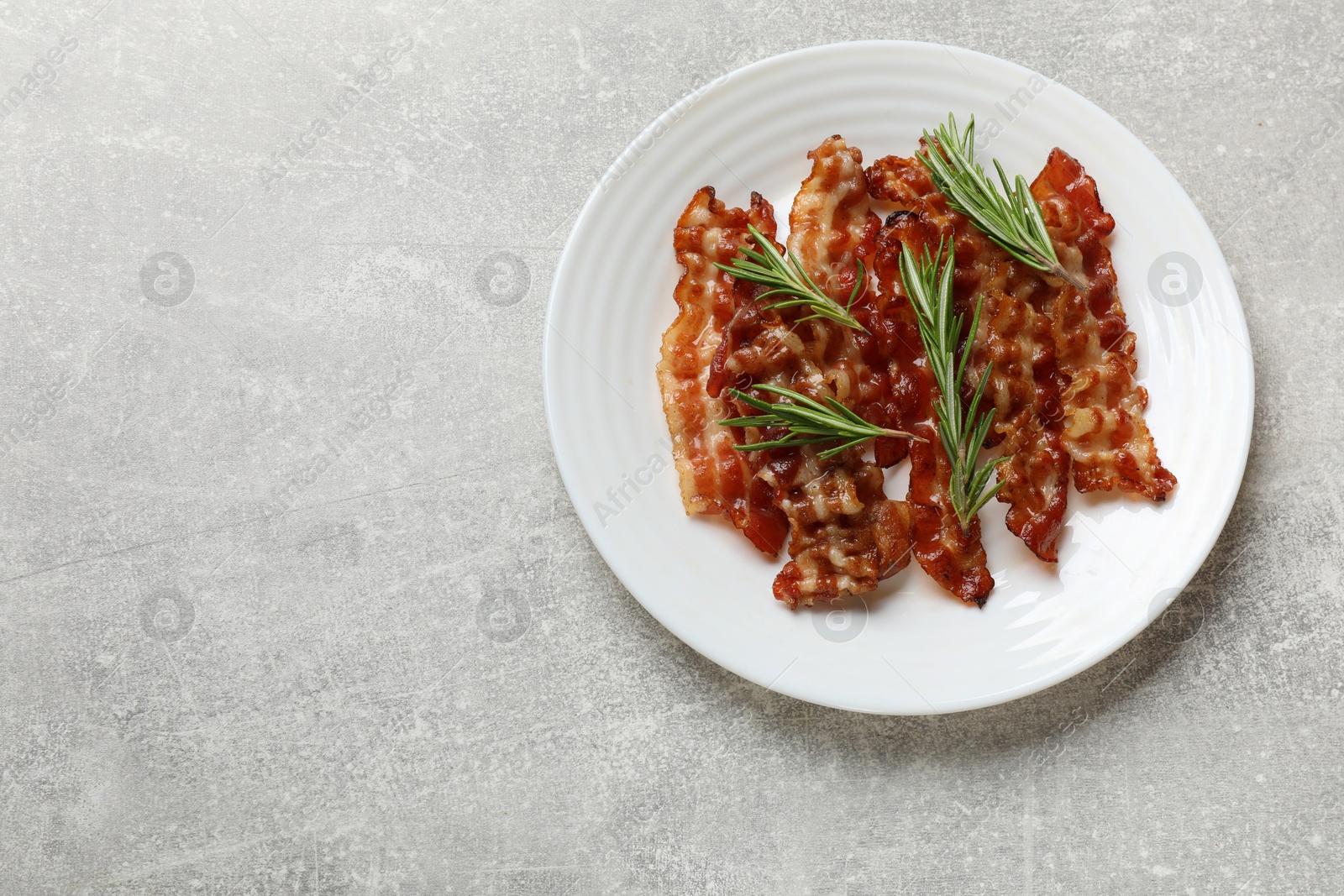 Photo of Slices of tasty fried bacon and rosemary on light grey table, top view. Space for text