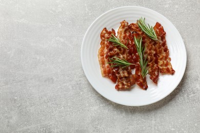 Photo of Slices of tasty fried bacon and rosemary on light grey table, top view. Space for text