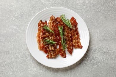 Photo of Slices of tasty fried bacon and rosemary on light grey table, top view