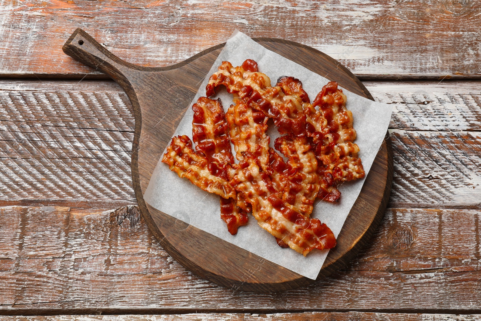 Photo of Slices of tasty fried bacon on wooden table, top view