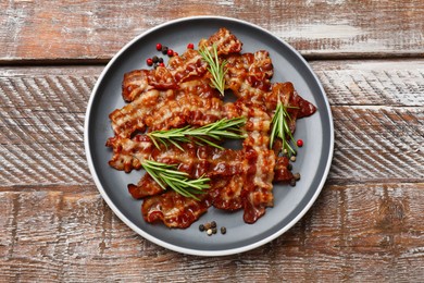 Photo of Slices of tasty fried bacon, peppercorns and rosemary on wooden table, top view