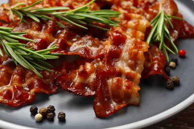 Photo of Slices of tasty fried bacon, peppercorns and rosemary on table, closeup