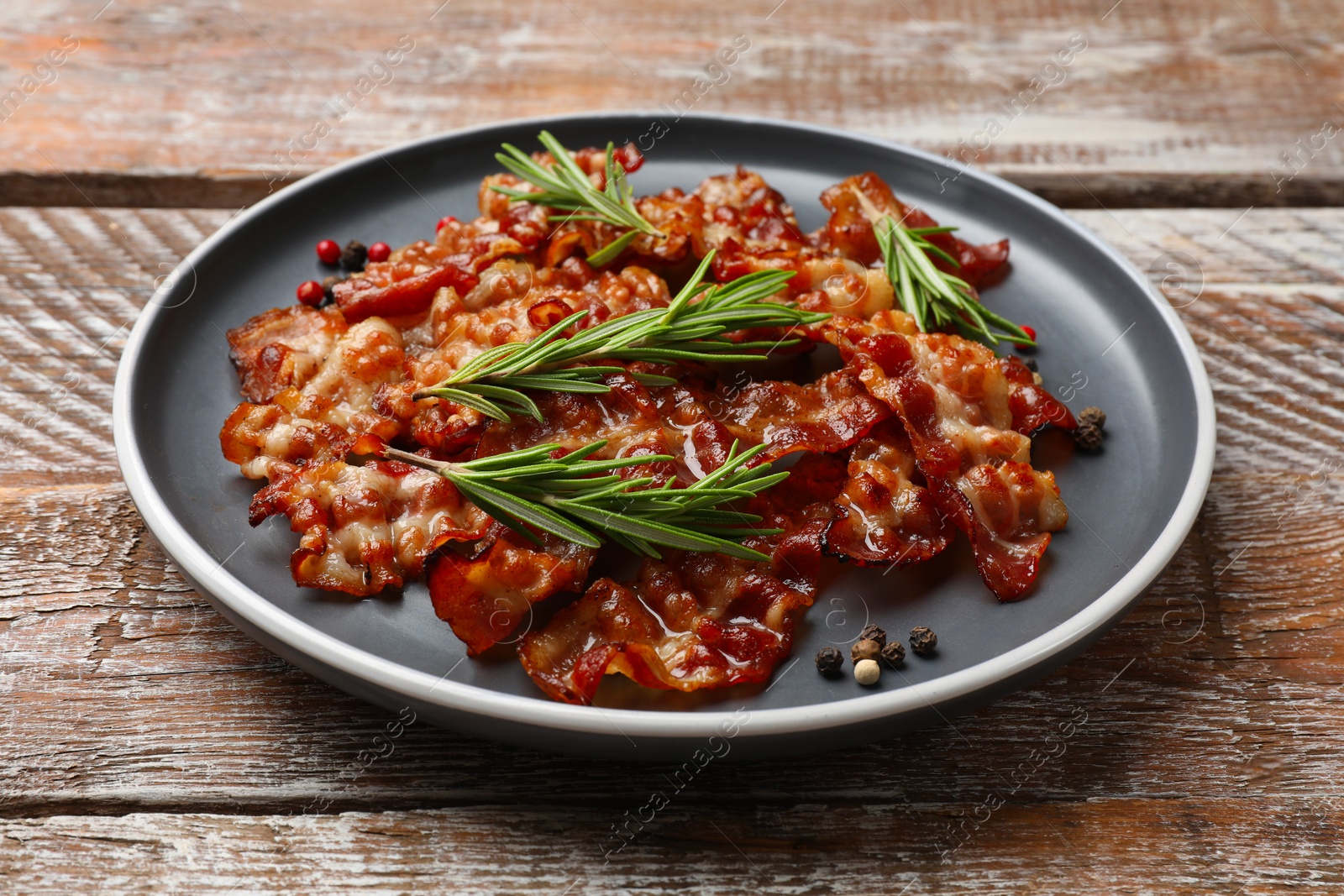 Photo of Slices of tasty fried bacon, peppercorns and rosemary on wooden table