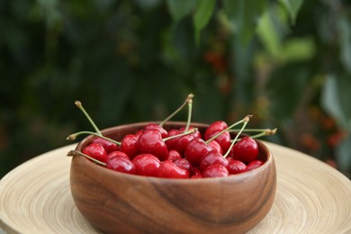 Photo of Tasty ripe red cherries in wooden bowl outdoors, space for text