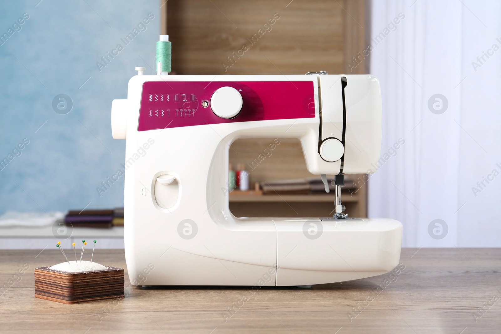 Photo of White sewing machine and pin cushion with needles on wooden table indoors