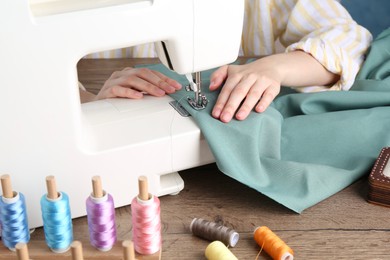 Photo of Seamstress working with sewing machine at wooden table indoors, closeup