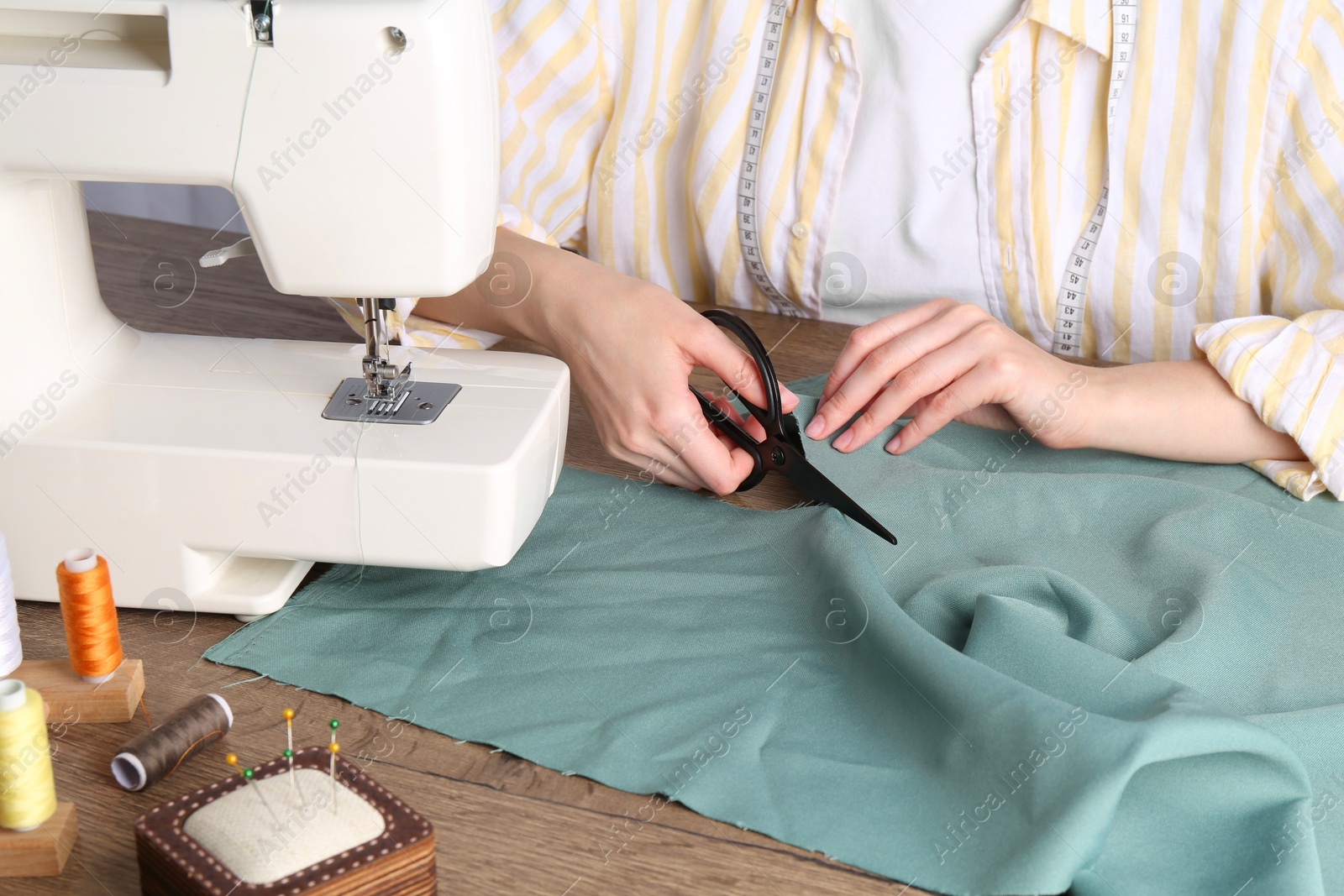 Photo of Seamstress cutting fabric at wooden table indoors, closeup