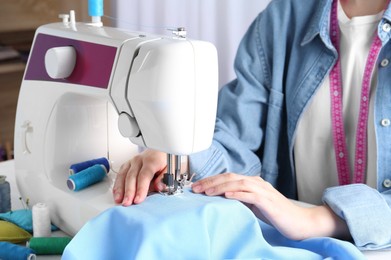 Photo of Seamstress working with sewing machine at table indoors, closeup