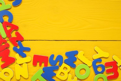 Learning alphabet. Magnetic letters on yellow wooden background, flat lay. Space for text